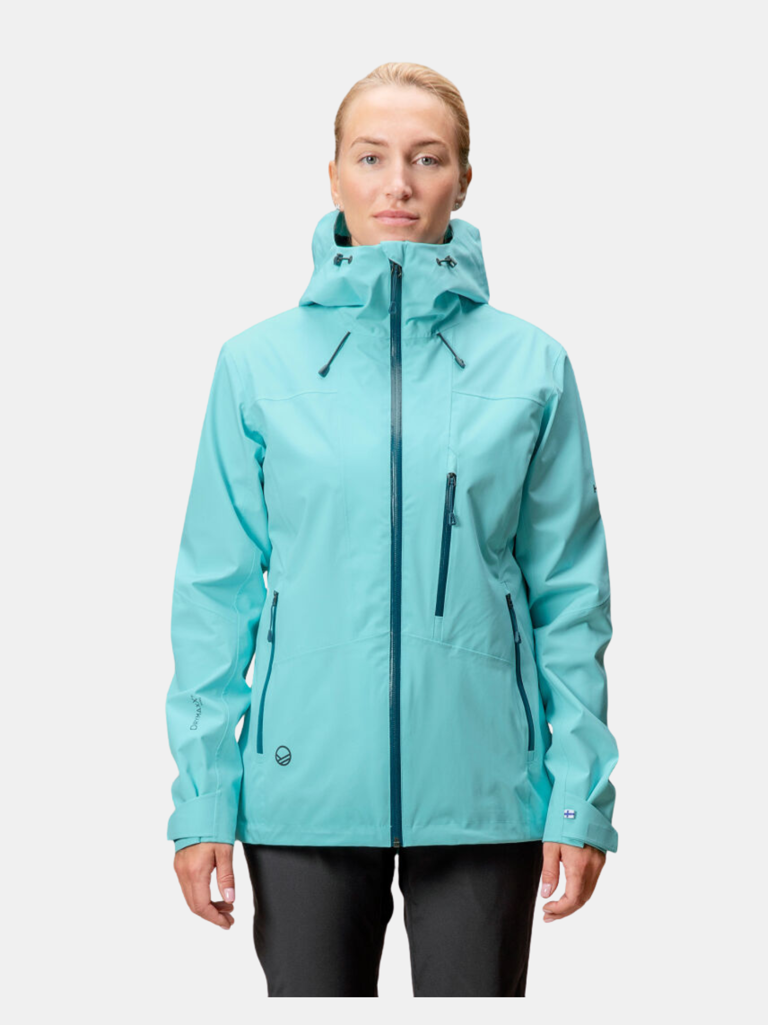 Henkilö seisoo kasvot menosuuntaan, yllään vaaleansininen hupullinen sadetakki, jossa on useita vetoketjullisia taskuja, ja mustat housut valkoista taustaa vasten.