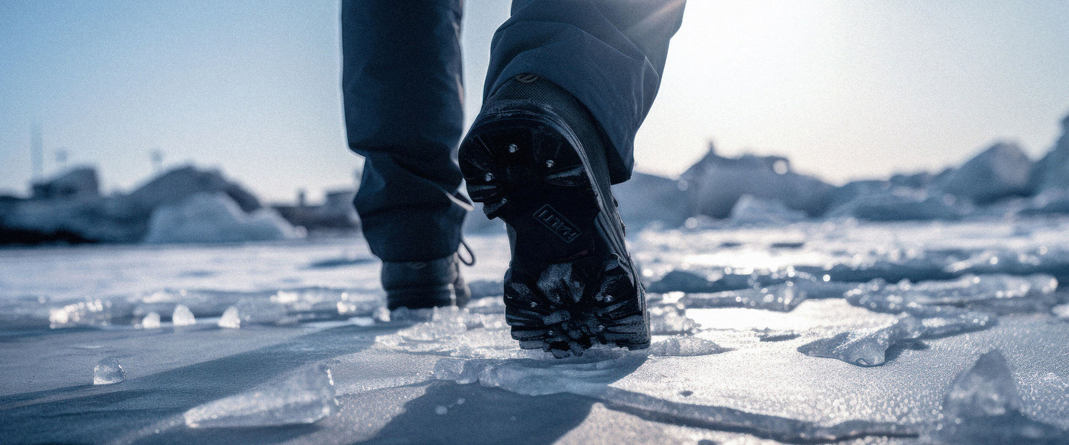 Lähikuva henkilöstä, joka kävelee jäällä tummissa housuissa ja tukevissa saappaissa. Taustalla näkyy jäinen maisema, jossa on hajanaisia jääpaloja ja kirkas taivas.