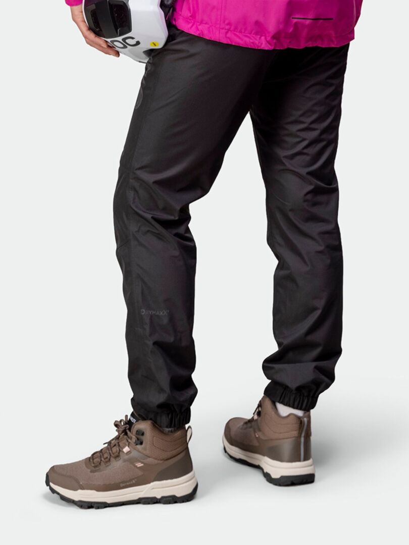 Henkilö mustissa housuissa ja Halti Fara 3 DX Mid Ulkoilukenkä Naisten, kypärä kädessä vaaleaa taustaa vasten.