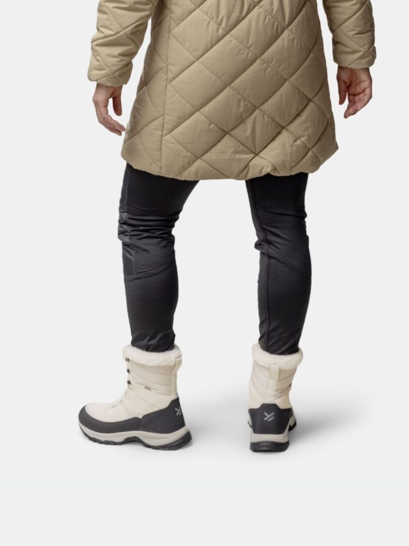 Henkilö, jolla on beige tikattu takki, mustat housut ja valkoiset Halti Tornio 2 DX Talvikenkä -saappaat, kuvattu takaa.