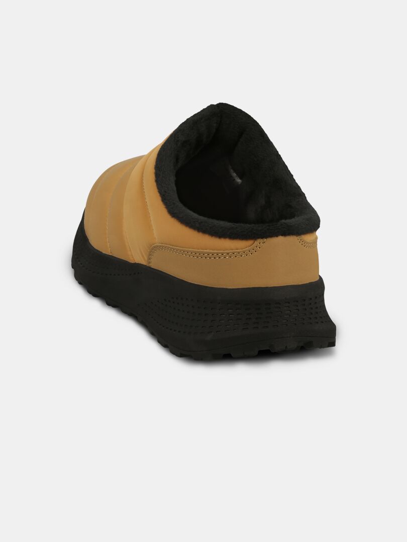 Halti Rest 2 -tossut: vaaleanruskeat slip-on-tossut, joissa on musta pohja ja muistivaahtomuovi; kuvassa takapuolelta vaaleaa taustaa vasten.
