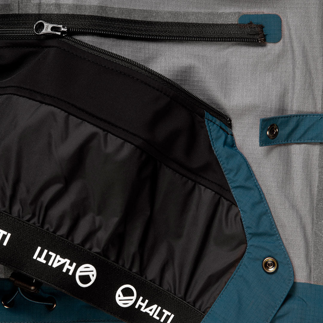 Lähikuva Alpine 3L DX Kuoritakki Unisex sisätilasta, jossa musta vetoketjutasku, sininen reunus ja Halti-brändi kuminauhassa.