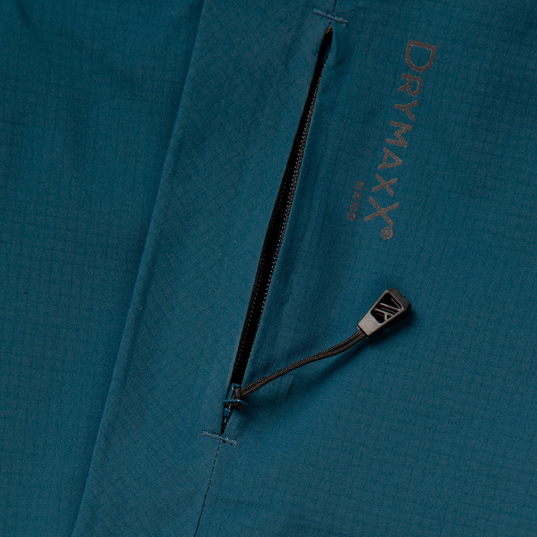 Lähikuva Halti Alpine 3L DX Kuoritakki Unisex -mallistosta, jossa on vetoketjullinen tasku, musta vetoketju ja DRYMAXX-logo yläpuolella.