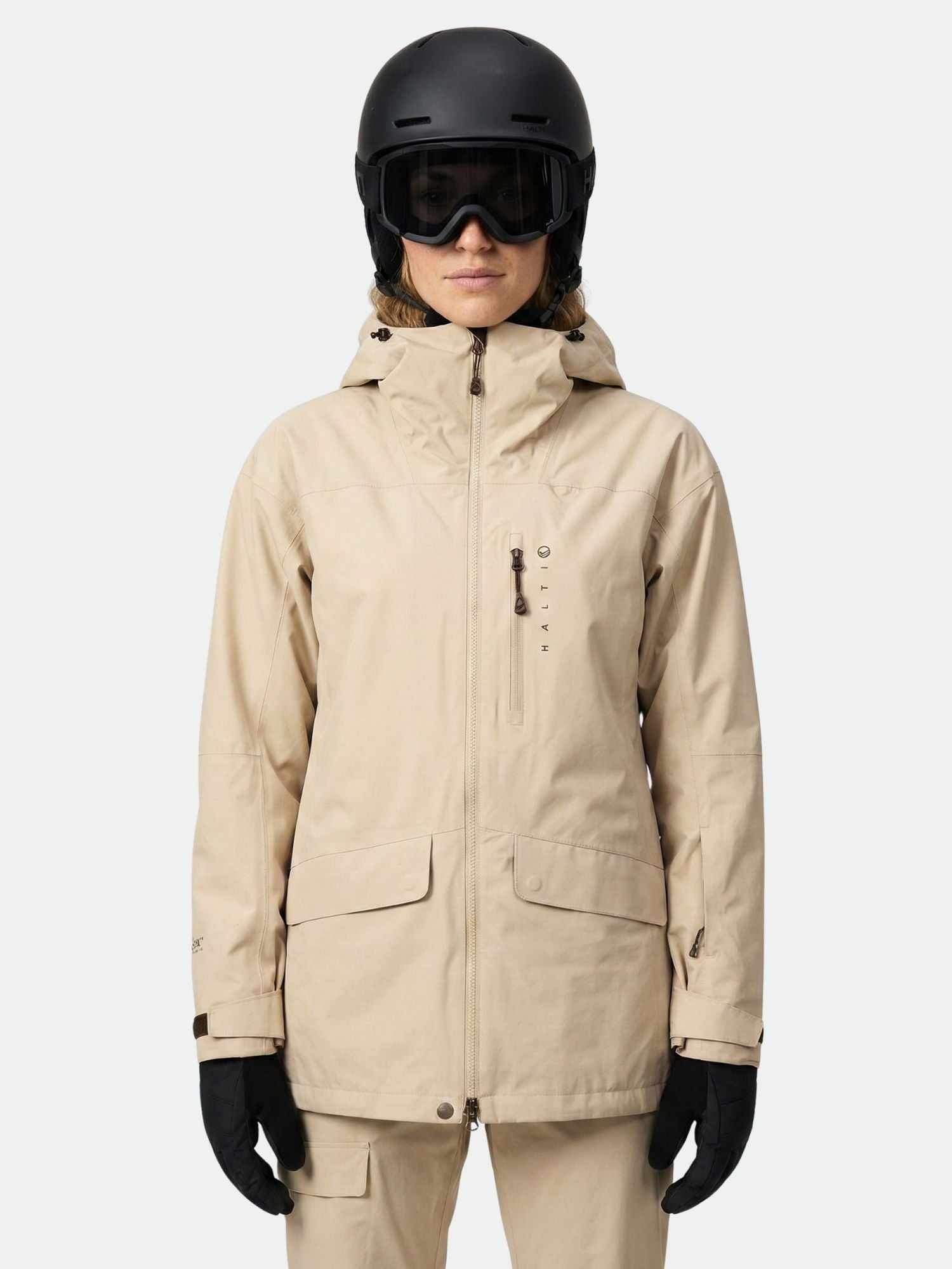 Henkilöllä beige Halti Settler 3L DX Laskettelutakki Naisten, yhteensopivat housut, mustat hanskat, hiihtolasit ja kypärä.