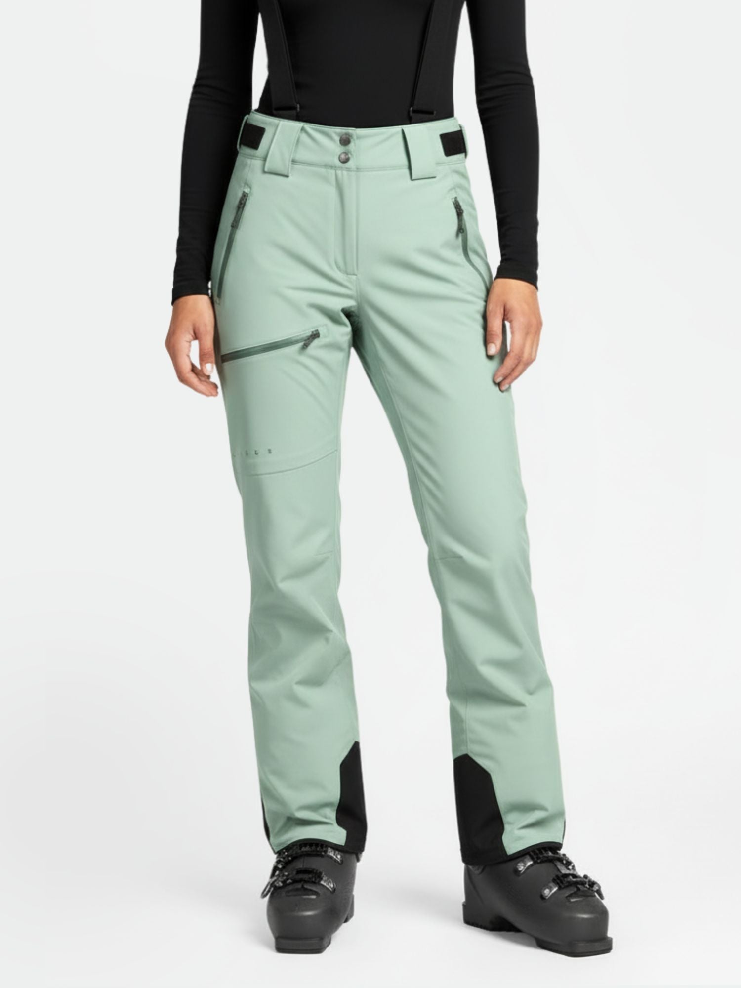 Henkilöllä on yllään Halti Carvey DrymaxX Naisten lasketteluhousut, musta toppi ja hiihtokengät valkoista taustaa vasten.