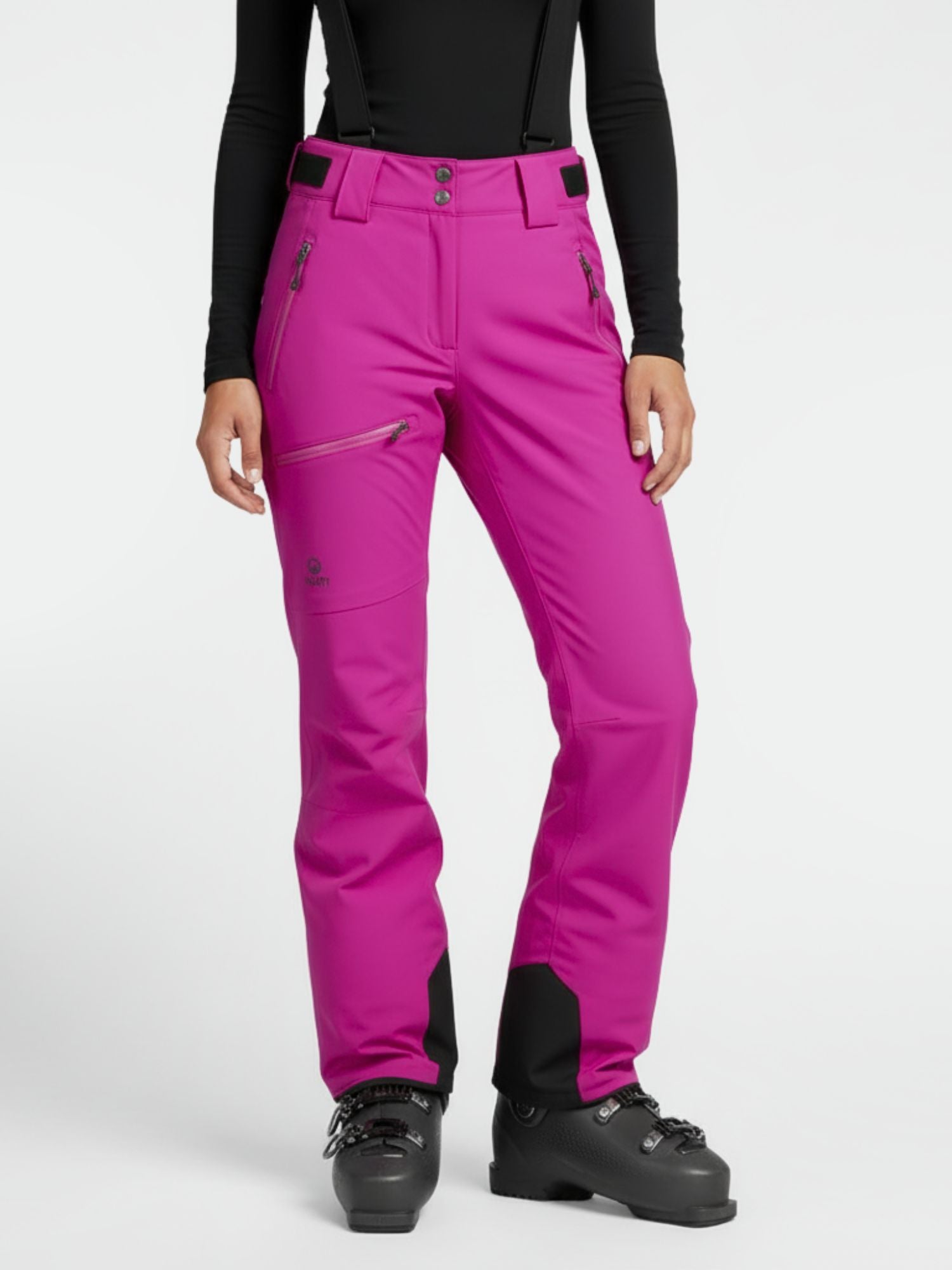 Henkilöllä on yllään kirkkaan vaaleanpunainen Halti Carvey DrymaxX Lasketteluhousut Naisten, musta toppi ja hiihtokengät valkoista taustaa vasten.