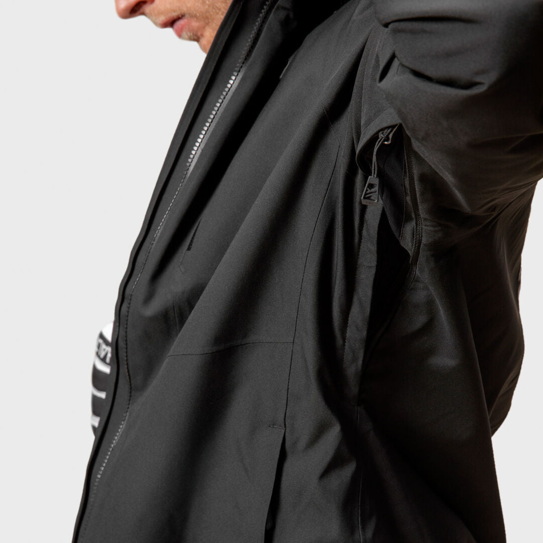 Mies mustassa Halti Vertica DX Laskettelutakissa näyttää kainalon vetoketjun aukkoa, osittain auki, tavallisella taustalla.