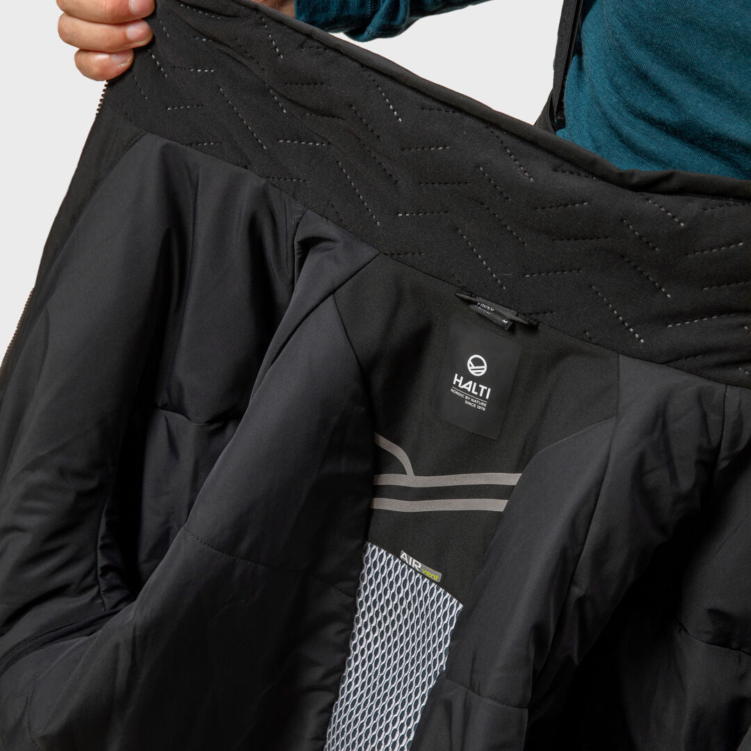 Henkilö pitää auki mustaa Halti Vertica DX Laskettelutakki Miesten, jossa näkyy Primaloft-toppaus ja tuotemerkin etiketti sisällä.