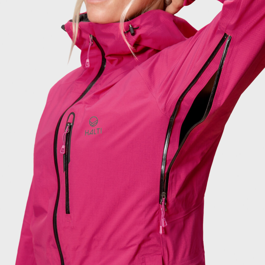 Henkilö kirkkaan vaaleanpunaisessa Halti Alpine 3L DX Kuoritakki Naisten, kuvassa leuasta vyötärölle, vetoketjulliset kainalo- ja rinta-aukotukset.