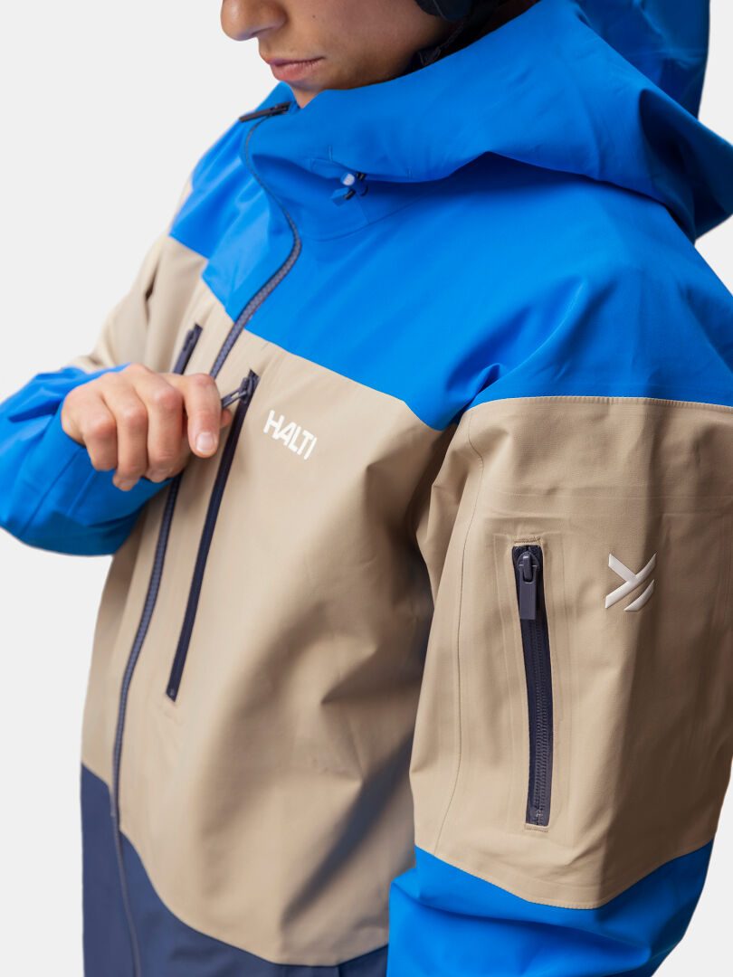 Henkilö vetoketjulla sininen ja beige Halti Rizle 3L DX Unisex laskettelutakki Primaloft Thermo fleece ja vetoketjutaskut.