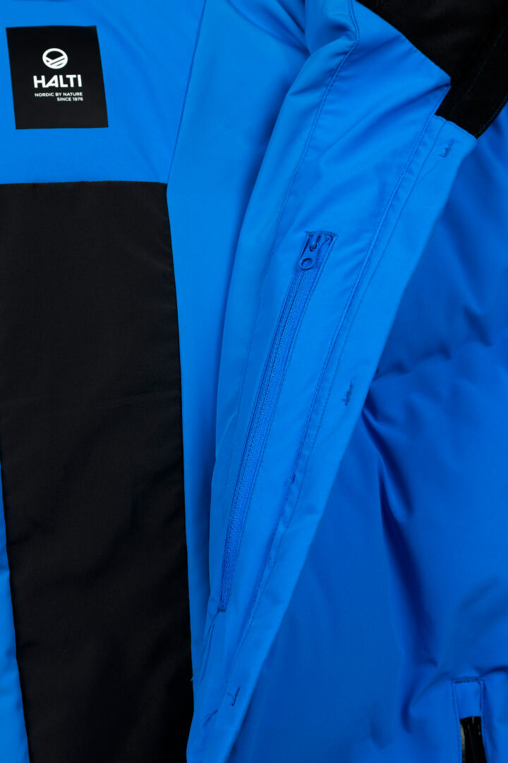 Lähikuva sinisestä Halti Nordic Arcty II miesten laskettelutakista, jossa on vetoketjullinen sisätasku ja Halti-logo vuorauksessa.