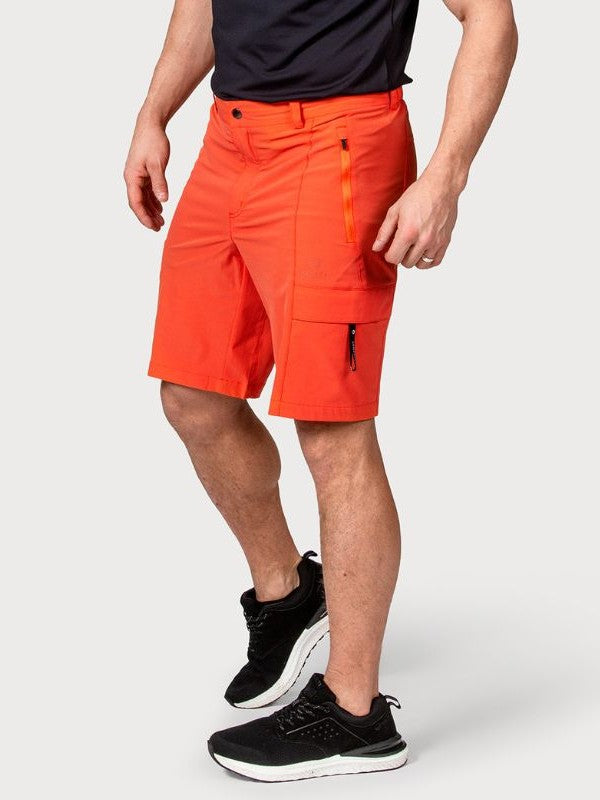 Joku pukeutuu Halti Reissu Miesten Stretch Shortsit kirkkaan oranssiin, mustaan paitaan ja mustiin kenkiin.