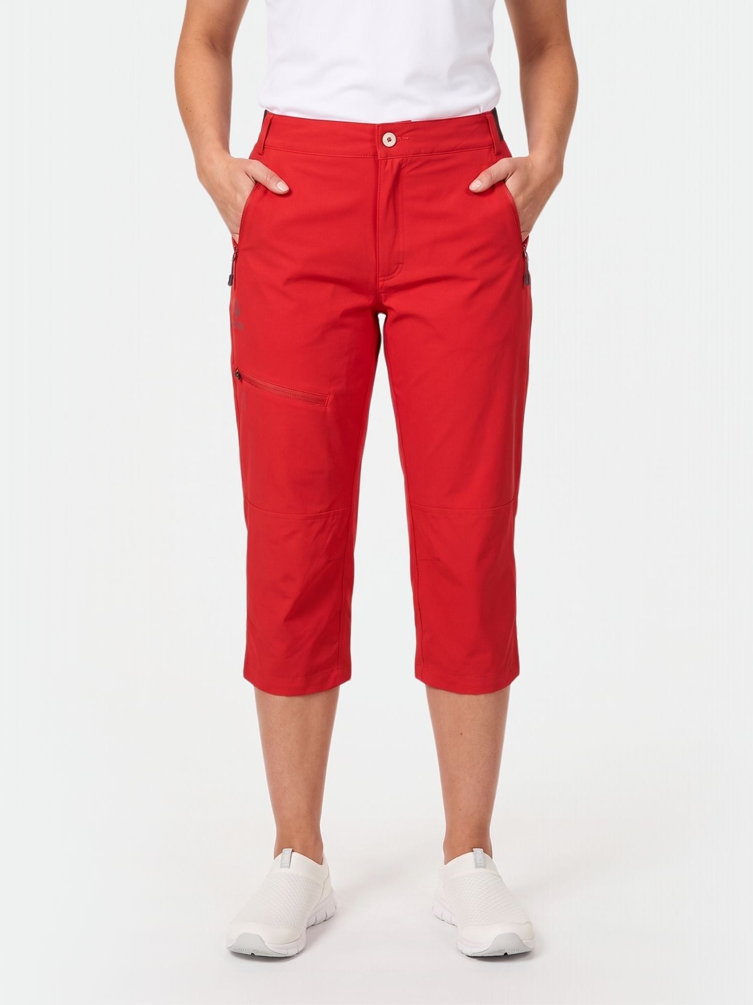 Henkilöllä on yllään punainen Halti Pallas Plus Naisten X-stretch Lite Caprit, valkoinen t-paita ja valkoiset slip-on-kengät, kädet taskuissa.
