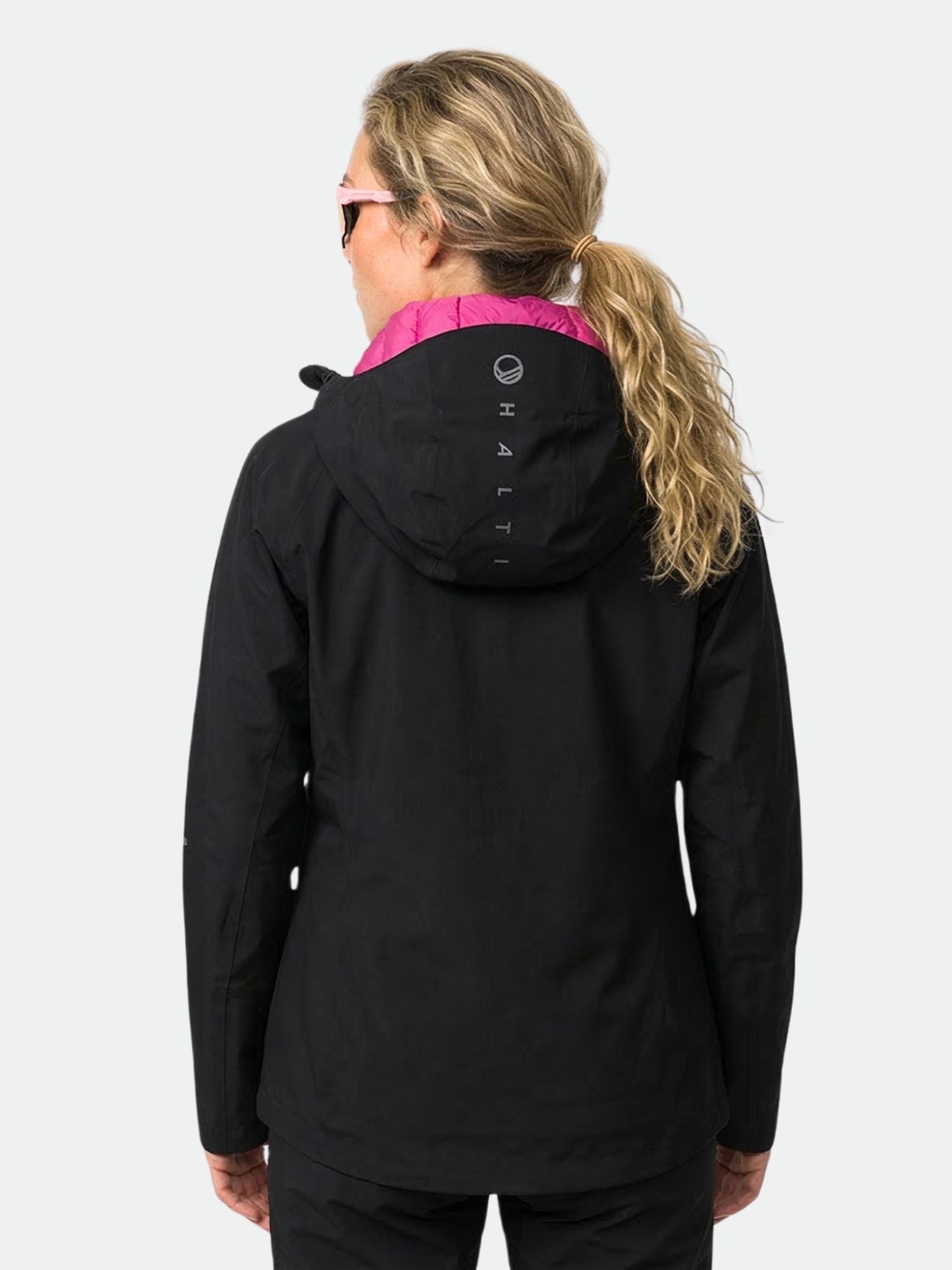 Nainen, jolla on vaalea aaltoileva poninhäntä, pukeutuu Halti Kaarna DX 3L -takkiin, jossa on vaaleanpunainen vuori ja HALTI-teksti hupussa.