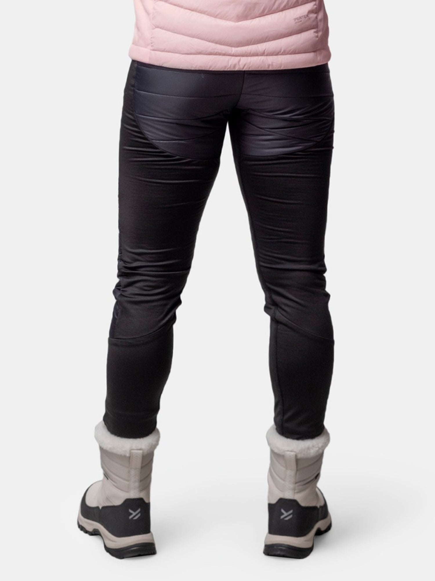 Henkilöllä on yllään Halti Veidnes Kevyesti Topatut Housut Naisten ja vaaleanharmaat talvisaappaat, takaa katsottuna valkoisella.