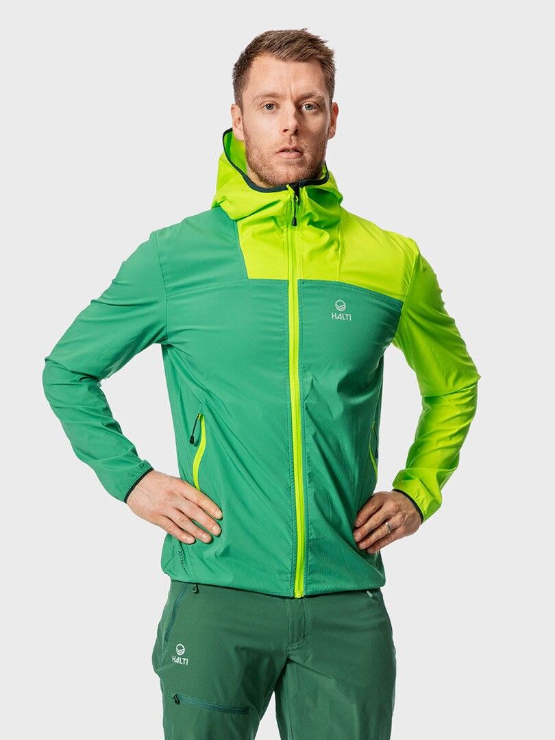 Halti Pallas Miesten Lite X-stretch -ulkoilutakki päällä oleva mies seisoo kädet lanteilla tavallista taustaa vasten.