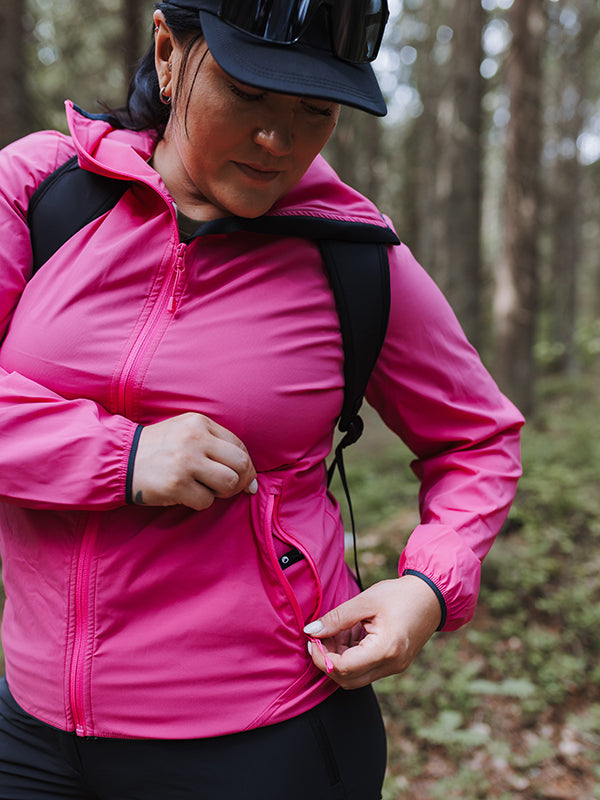 Nainen Halti Pallas Plus Naisten X-stretch Lite ulkoilutakissa avaa taskun metsässä, reppu yllään.