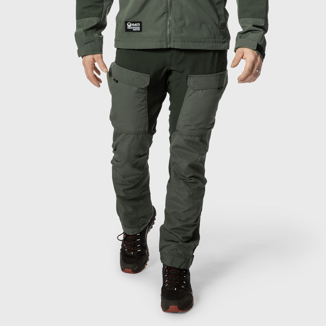 Henkilö, jolla on tummanvihreät rahtitaskuhousut, yhteensopiva takki ja mustat vaelluskengät, kuvattu vyötäröstä alaspäin.