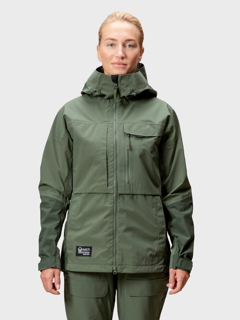 Päällään oliivinvärinen Halti Hiker DrymaxX 3L Ventilated Retkeilytakki Naisten ja siihen sopivat housut, yksiväristä taustaa vasten.