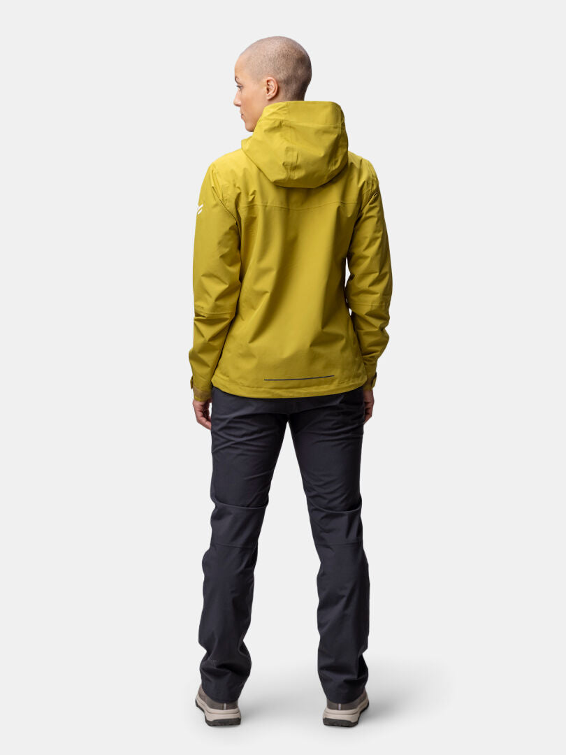 Lyhythiuksisella henkilöllä on keltainen Halti Forter DX Kuoritakki Naisten ja tummat housut, kasvot poispäin valkoisella.