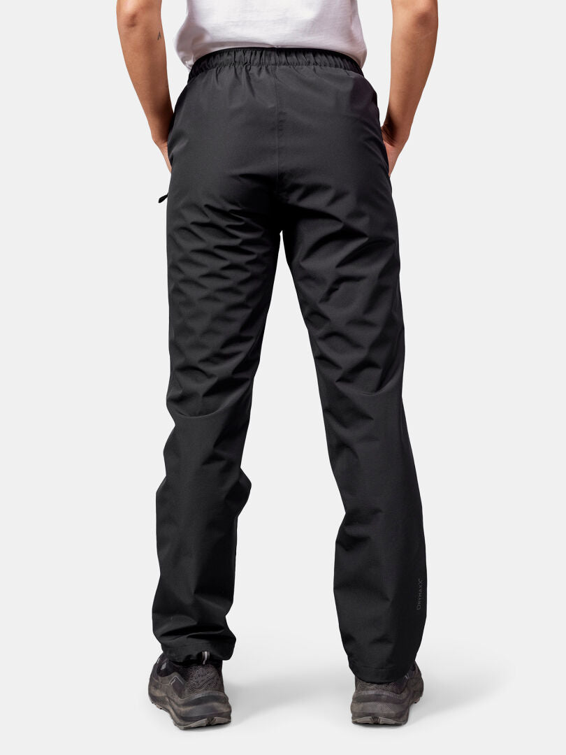 Henkilöllä on yllään Halti Forter DX Kuorihousut Naisten ja mustat vaelluskengät, kuvattu takaapäin vaaleaa taustaa vasten.