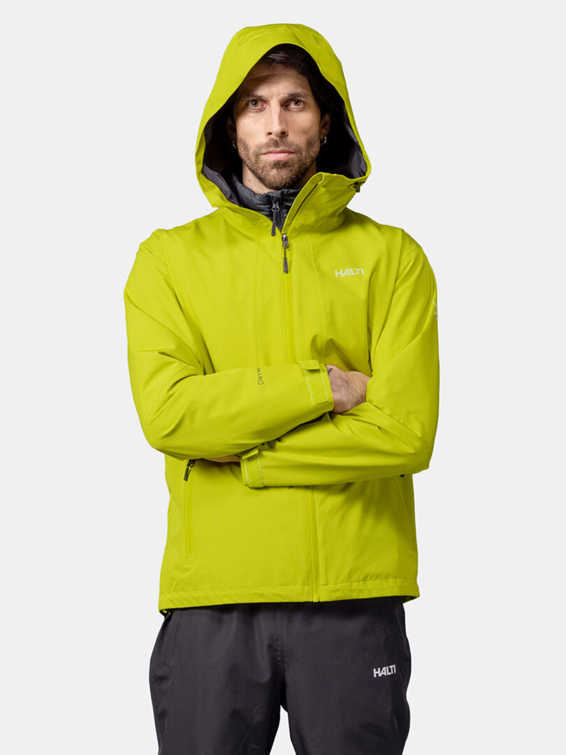 Mies kirkkaankeltaisessa Halti Forter DX Kuoritakki Miesten ja mustissa housuissa seisoo kädet ristissä.