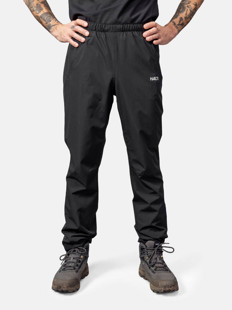 Henkilö, jolla on yllään Halti Forter DX Kuorihousut Miesten, vaelluskengät ja musta paita, seisoo kädet lanteilla.