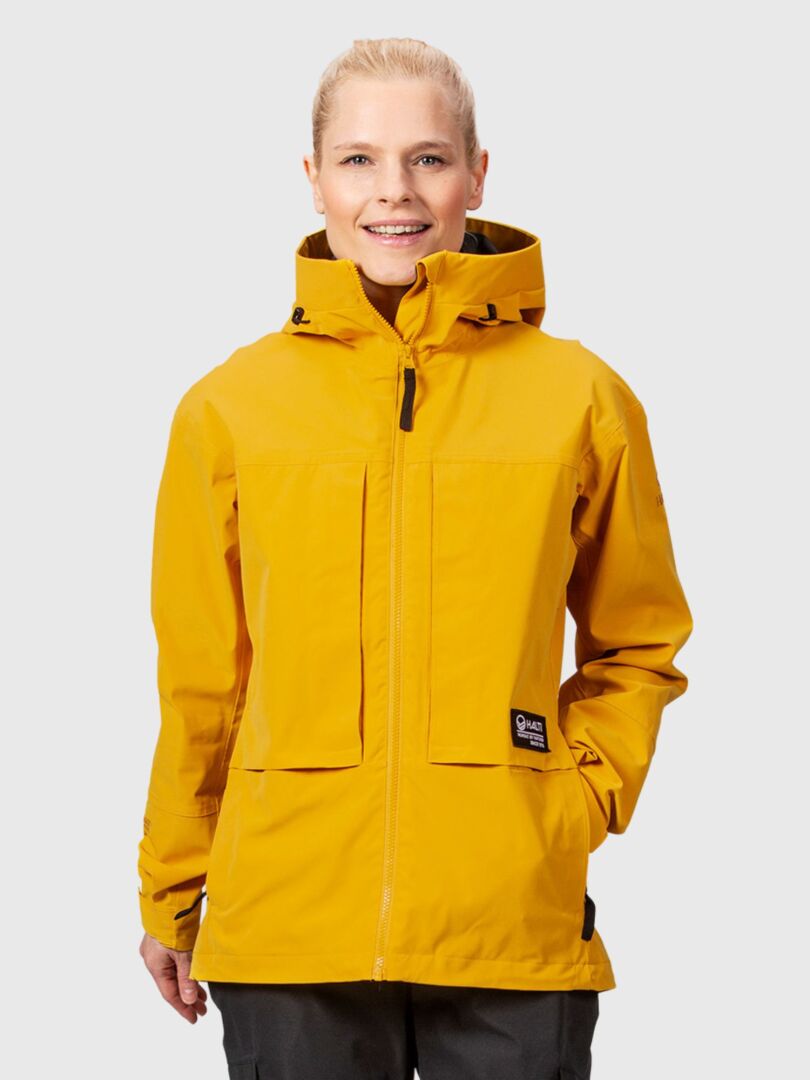 Henkilö, jolla on yllään kirkkaankeltainen Halti Hiker II DrymaxX Kuoritakki Naisten, täydellinen retkeilyyn, vaaleanharmaalla taustalla.