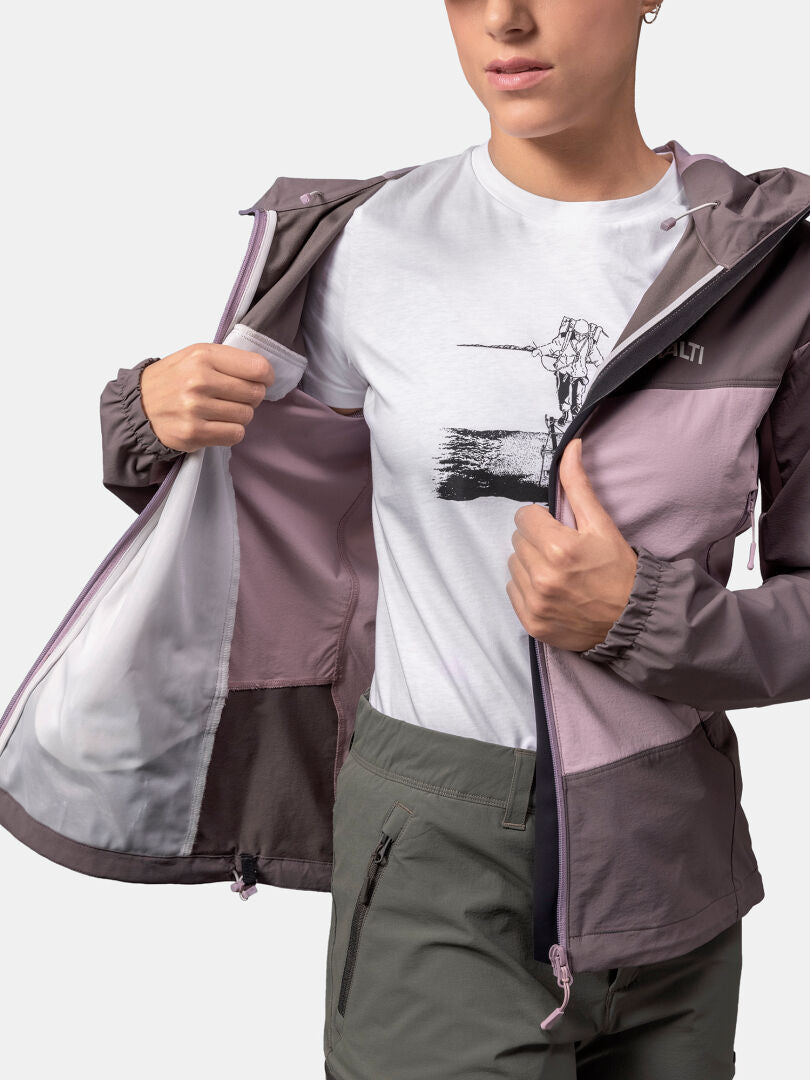 Henkilö avaa Halti Pallas Evo X-stretch Takki Naisten vetoketjun ja paljastaa valkoisen graafisen t-paidan ja oliivinvihreät housut.