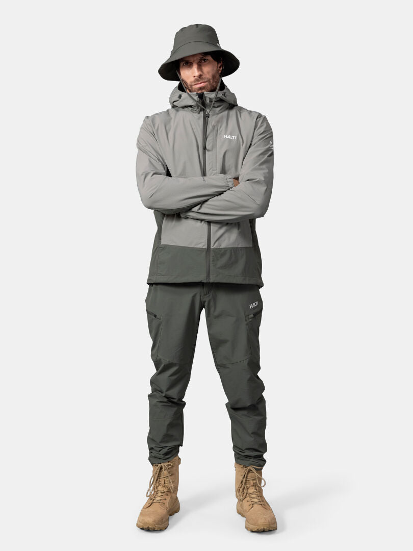Miehellä on harmaa Halti Pallas Evo X-stretch takki, kädet ristissä valkoista taustaa vasten.