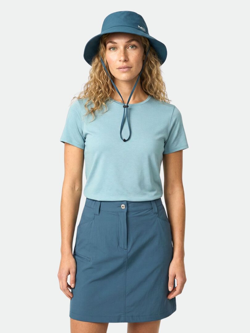 Nainen seisoo kasvot menosuuntaan sinisessä pipossa, vaaleansinisessä t-paidassa ja Halti Pallas Cool Shortsihame naisten.