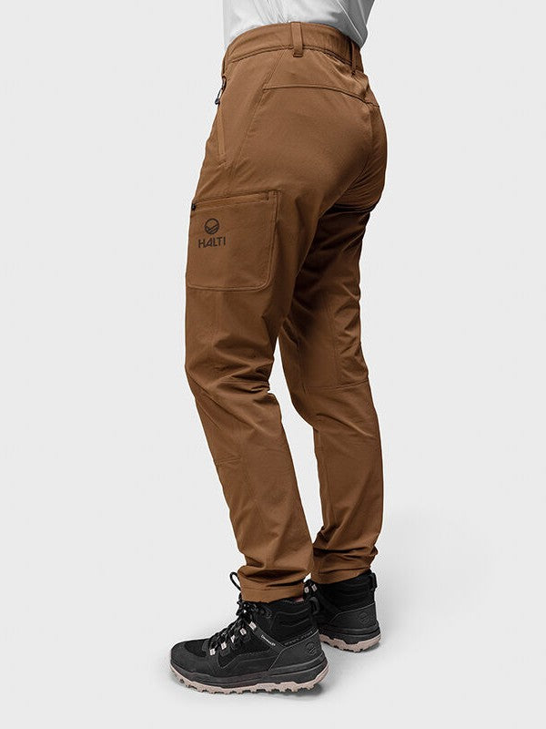 Henkilöllä Halti Pallas Evo Brushed X-stretch Ulkoiluhousut Naisten ja mustat vaelluskengät vaaleaa taustaa vasten.