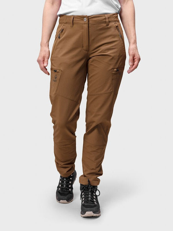 Henkilöllä on yllään ruskeat Halti Pallas Evo Brushed X-stretch Ulkoiluhousut Naisten, valkoinen paita ja mustat vaelluskengät.