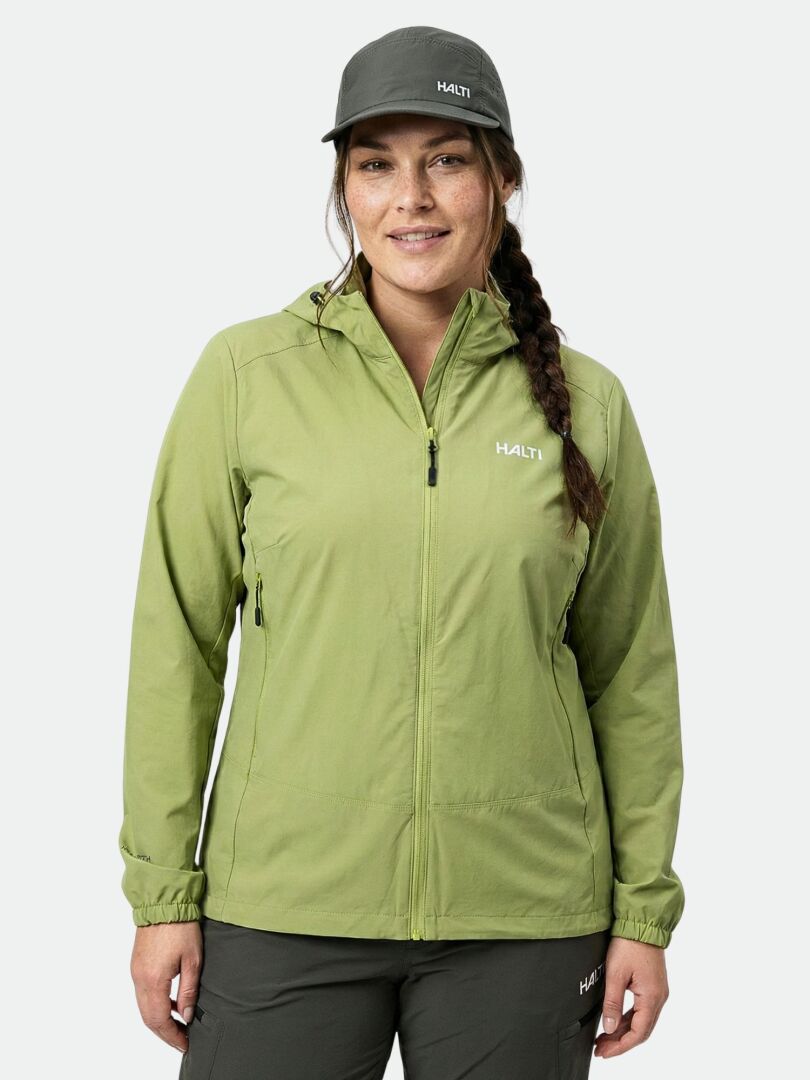 Naisella on yllään vihreä Halti Pallas Evo Plus X-stretch -takki ja harmaa lippis, joissa molemmissa on Halti-logot, kameraan päin.
