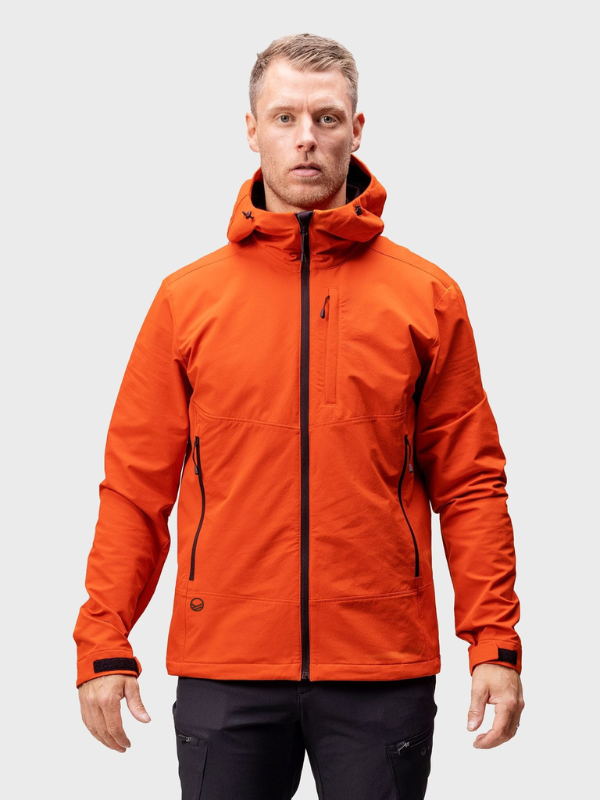 Miehellä on Halti Pallas Evo Brushed X-stretch Takki Miesten ja mustat housut, seisoo vaaleanharmaata taustaa vasten.