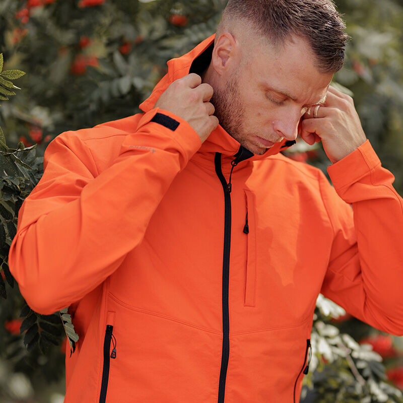 Mies Halti Pallas Evo Brushed X-stretch -takissa. Takki seisoo ulkona säätämässä huppua lehtien oksien lähellä.