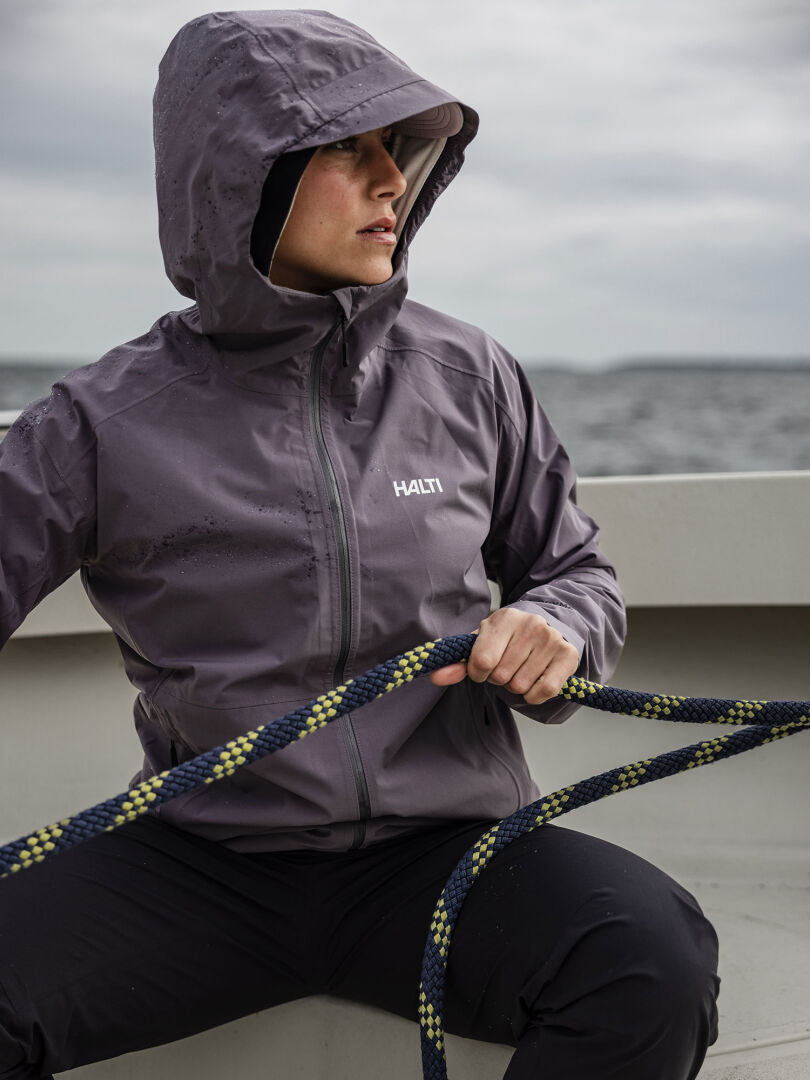 Halti Staala DX Kuoritakki Naisten henkilö pitää köyttä veneessä, jonka takana on vettä ja pilviä.