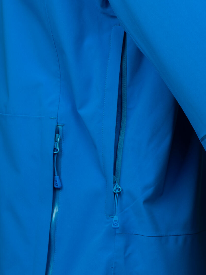 Lähikuva Halti Staala DX Kuoritakki Miesten vedenpitävästä miesten takista, jossa näkyy vetoketjulliset taskut ja kankaan rakenne.