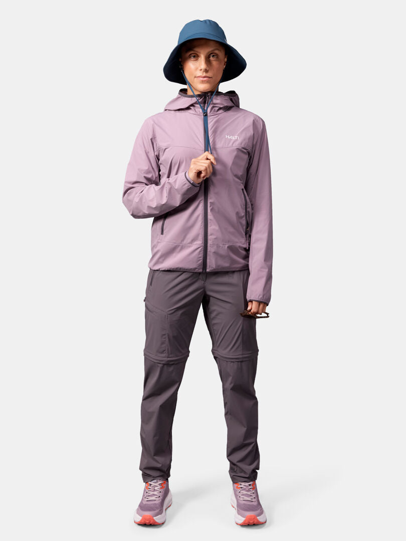 Henkilö katsoo eteenpäin sinisessä pipossa, Halti Pallas Cool X-stretch Takki, harmaat housut ja vaaleanpunaisella korostuksella varustetut lenkkarit.