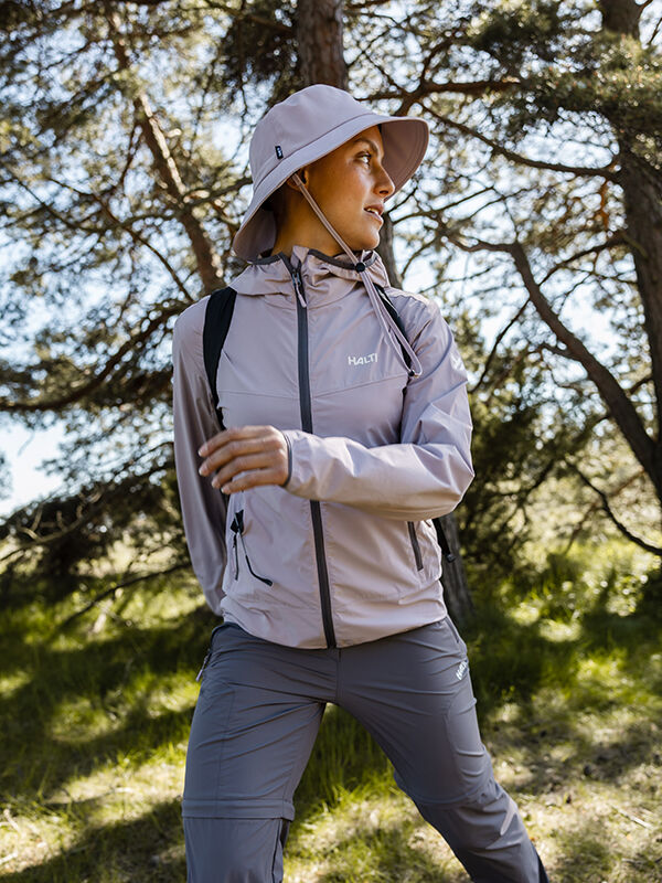 Halti Pallas Cool X-stretch Takki Naisten ja leveälippaiseen hattuun pukeutunut henkilö nauttii kesäisistä aktiviteeteista ulkona puiden keskellä.