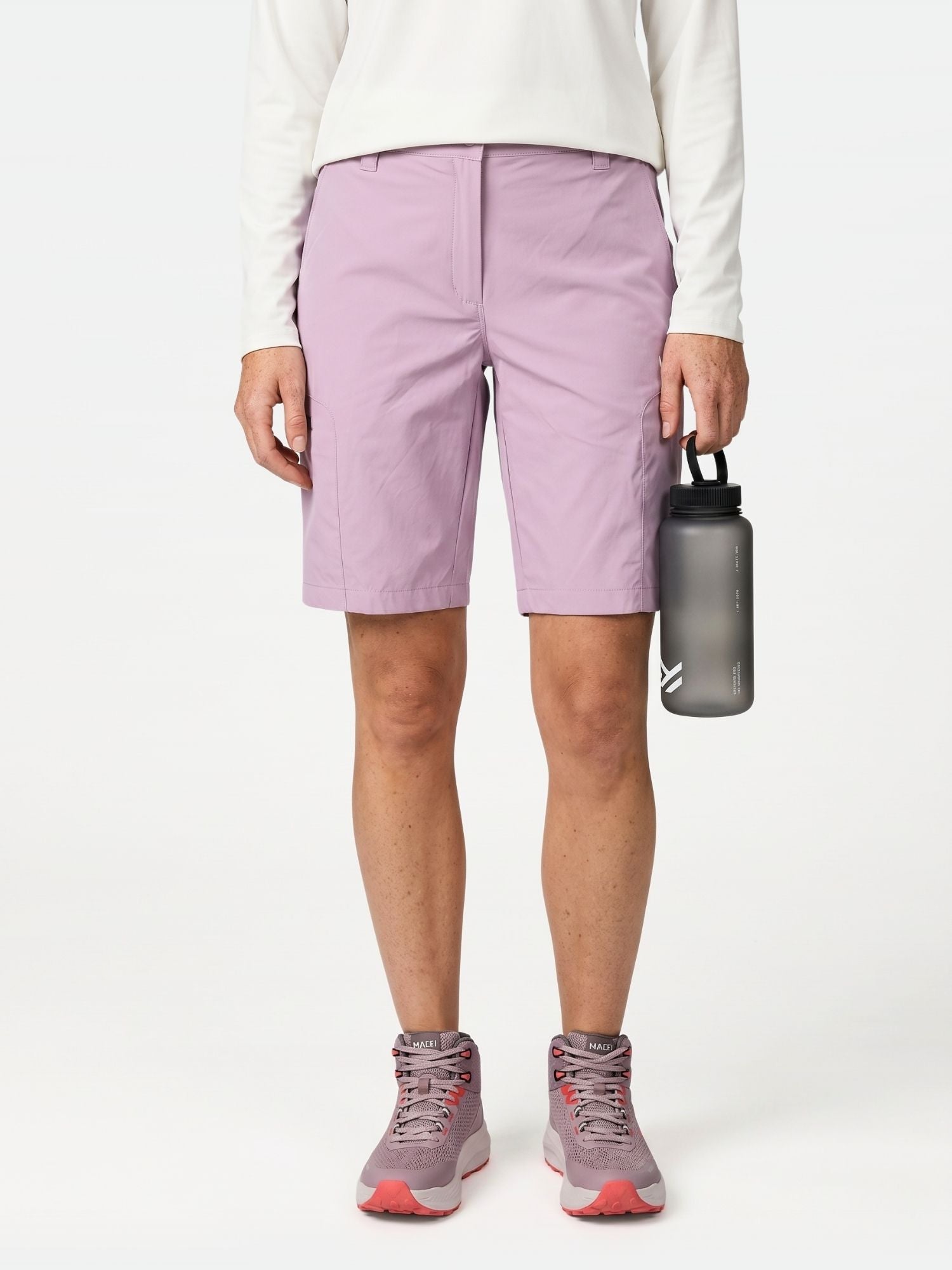 Henkilö, jolla on valkoinen pitkähihainen paita, Halti Pallas Cool Shortsit Naisten, violetit lenkkarit, kädessään harmaa vesipullo.