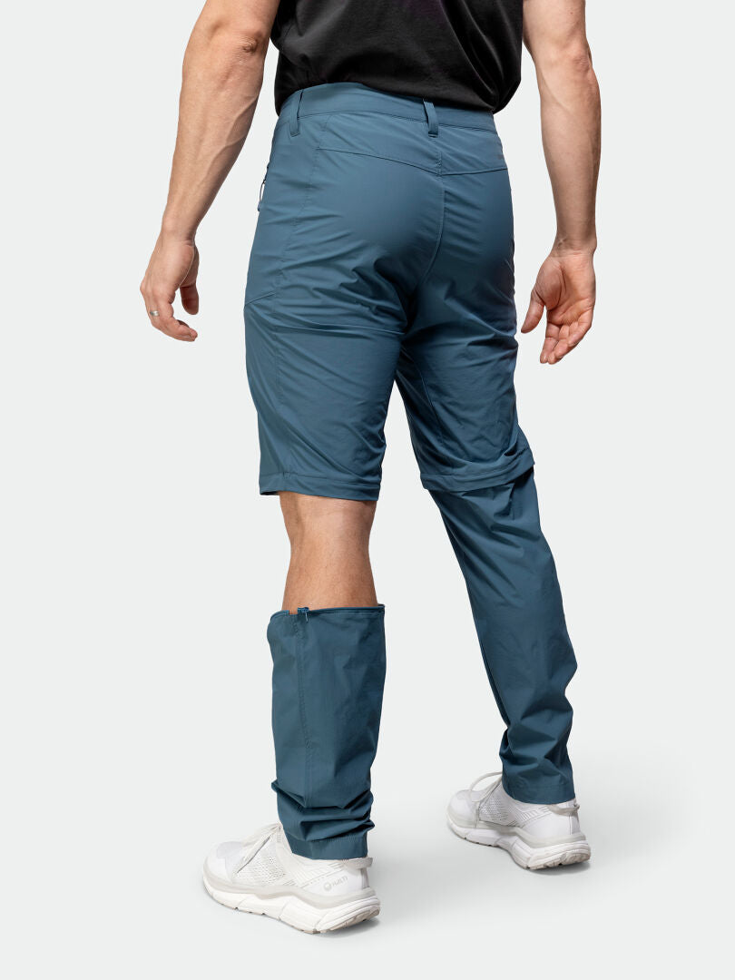 Henkilö, jolla on Halti Pallas Cool Stretch Zip-off Housut Miesten, josta on poistettu oikea jalka, valkoiset lenkkarit.