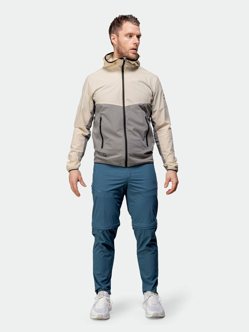 Mies, jolla on beige-harmaa hupparitakki, Halti Pallas Cool Stretch Zip-off -takki ja valkoiset lenkkarit, seisoo sivuttain.