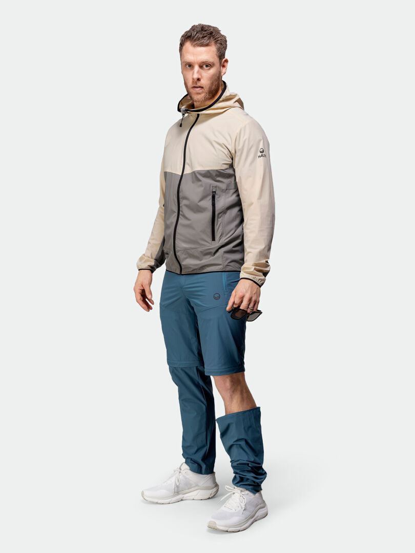 Mies, jolla on beige-harmaa hupullinen takki, Halti Pallas Cool Stretch Zip-off Housut Miesten ja valkoiset lenkkarit, seisoo.