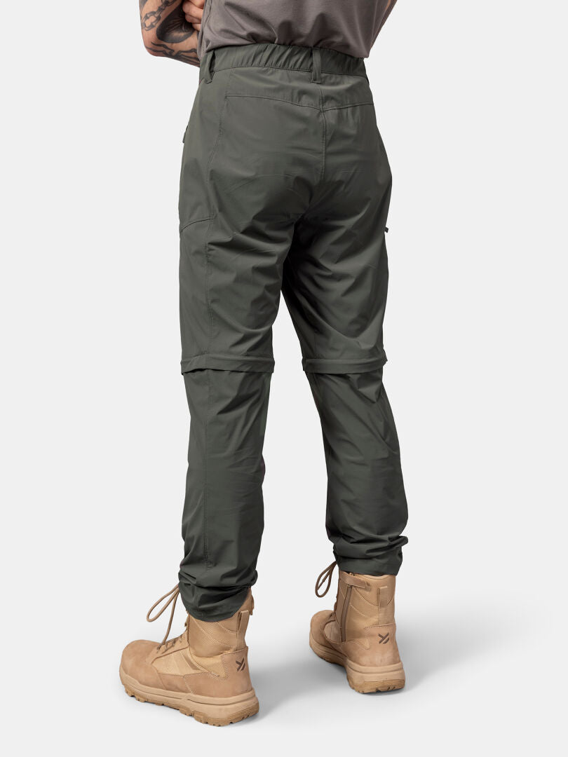 Henkilöllä on Halti Pallas Cool Stretch Zip-off Housut Miesten ja ruskeat nauhakengät valkoisella pohjalla.