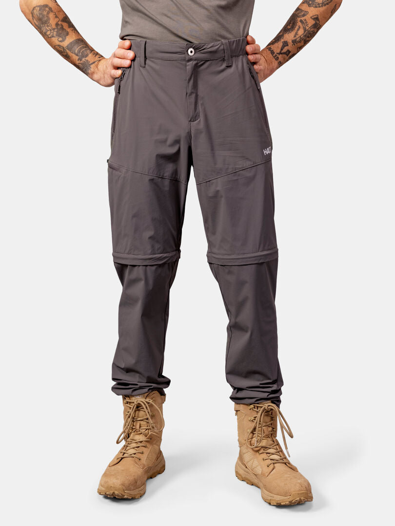 Henkilöllä on yllään Halti Pallas Cool Stretch Zip-off Housut Miesten ja ruskehtavat saappaat, seisoo kädet lanteilla.