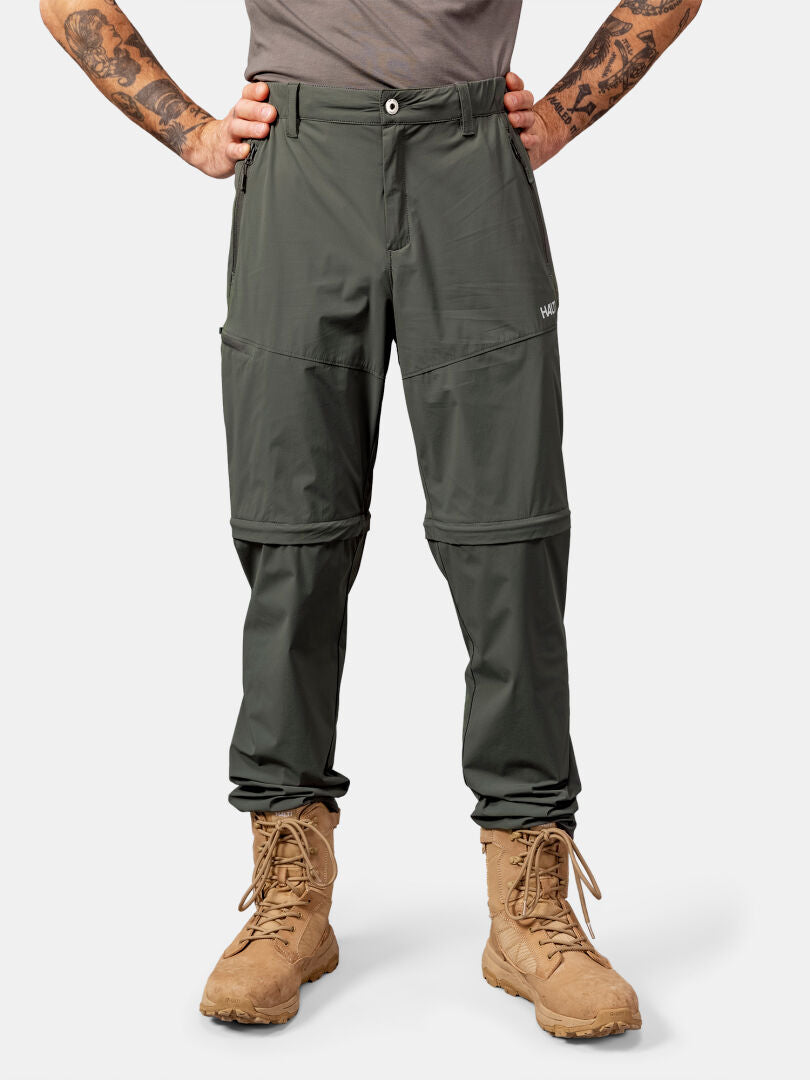 Henkilöllä on yllään Halti Pallas Cool Stretch Zip-off Housut Miesten ja ruskehtavat saappaat, seisoo kädet lanteilla.