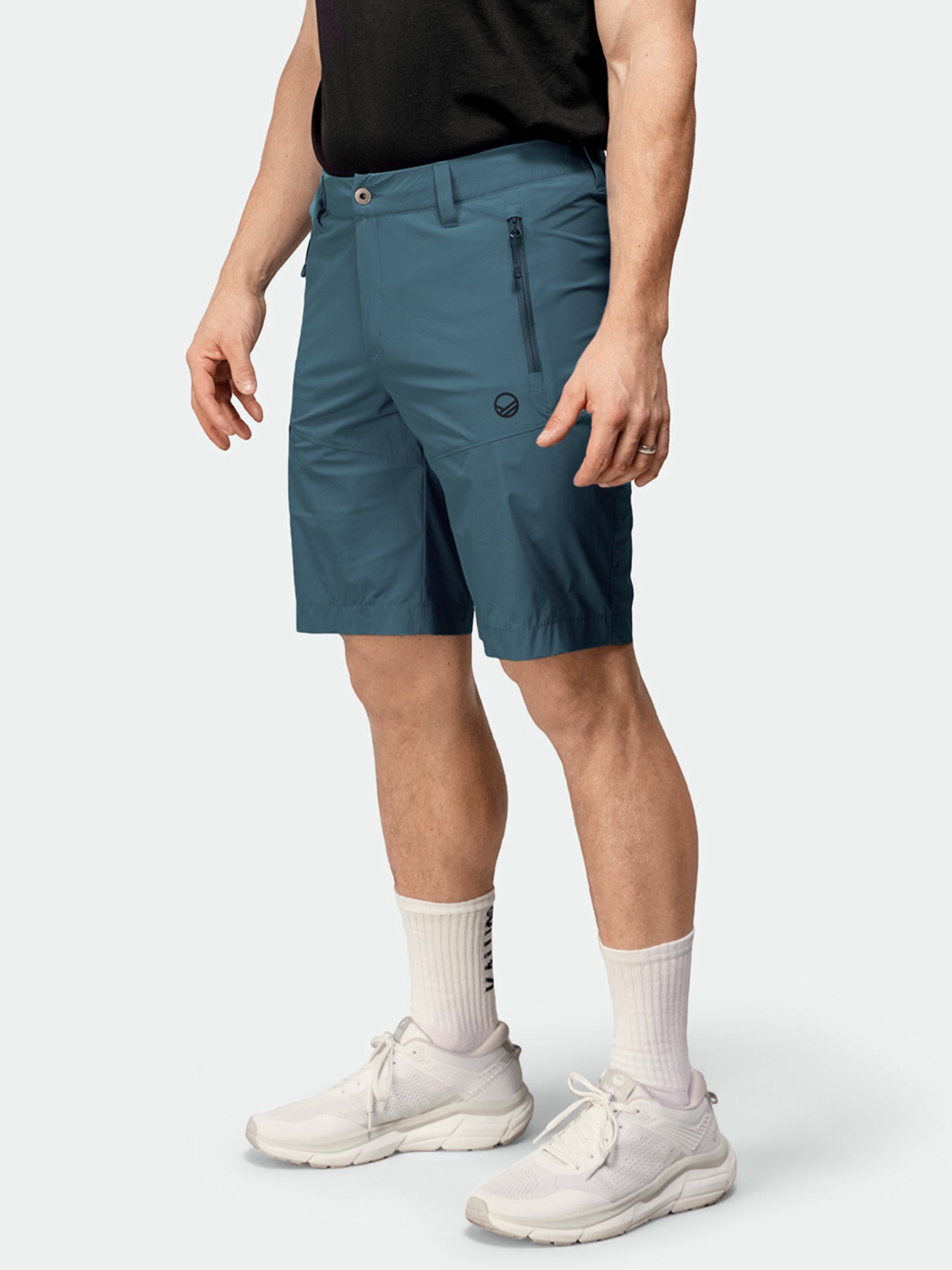 Jollakulla on yllään tiilenpunainen Halti Pallas Cool X-stretch Shortsit Miesten, musta paita, valkoiset sukat ja lenkkarit yksivärisellä pohjalla.