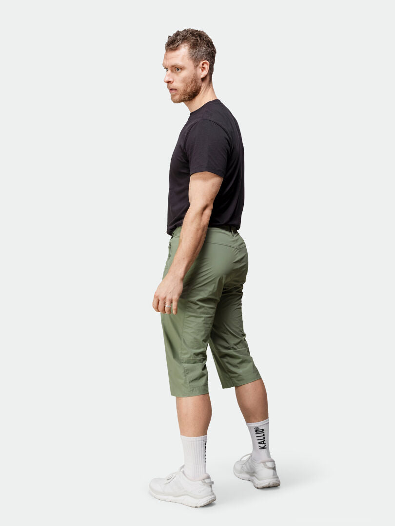 Mies seisoo kyljellään yllään musta t-paita, Halti Pallas Cool X-stretch Caprit Miesten takki, valkoiset sukat ja lenkkarit.