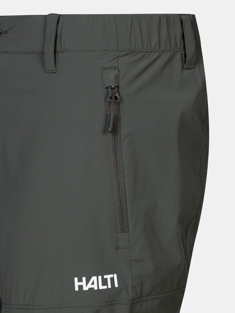 Lähikuva Halti Pallas Cool X-stretch Caprit Miesten -paidasta, jossa on vetoketjutasku, UPF 90+ ja valkoinen logo lähellä helmaa.